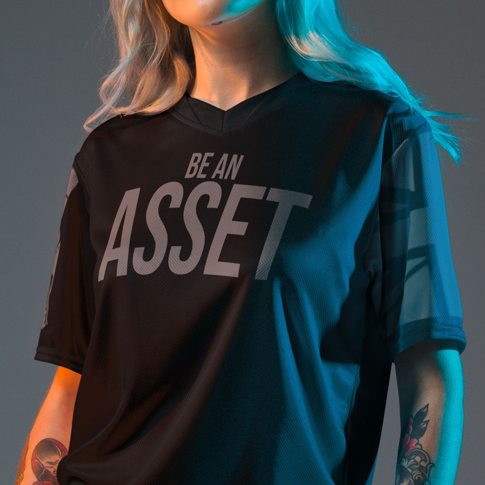 Close up of front of woman wearing black Activewear Achilles Tactical Clothing Brand short sleeve unisex T-shirt with BE AN ASSET printed across chest in original grey