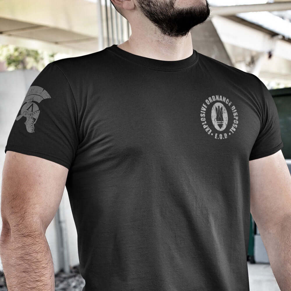 Close up of Man wearing Black short sleeve unisex fit cotton T-Shirt by Achilles Tactical Clothing Brand printed with Bomb Logo and Explosive Ordnance Disposal design across the Left Chest