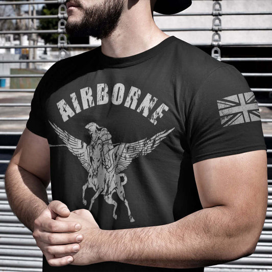 Close up of front of Man wearing Black cotton short sleeve unisex fit T-Shirt by Achilles Tactical Clothing Brand printed with Airborne and Pegasus design across the front chest